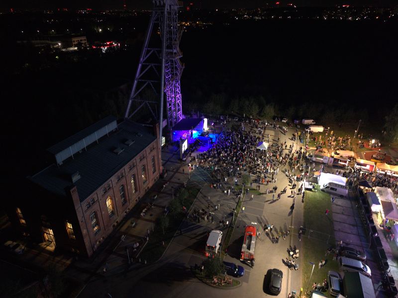 Podświetlony na fioletowo szyb kopalni, obok scena koncertowa i tłum ludzi nocą